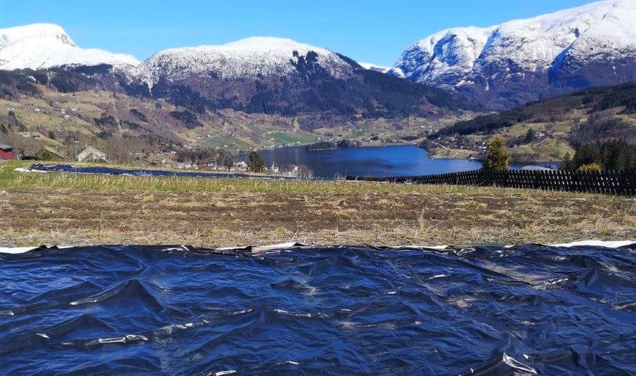Svart plast i forgrunnen, med fjell og landskap med blå himmel i bakgrunnen
