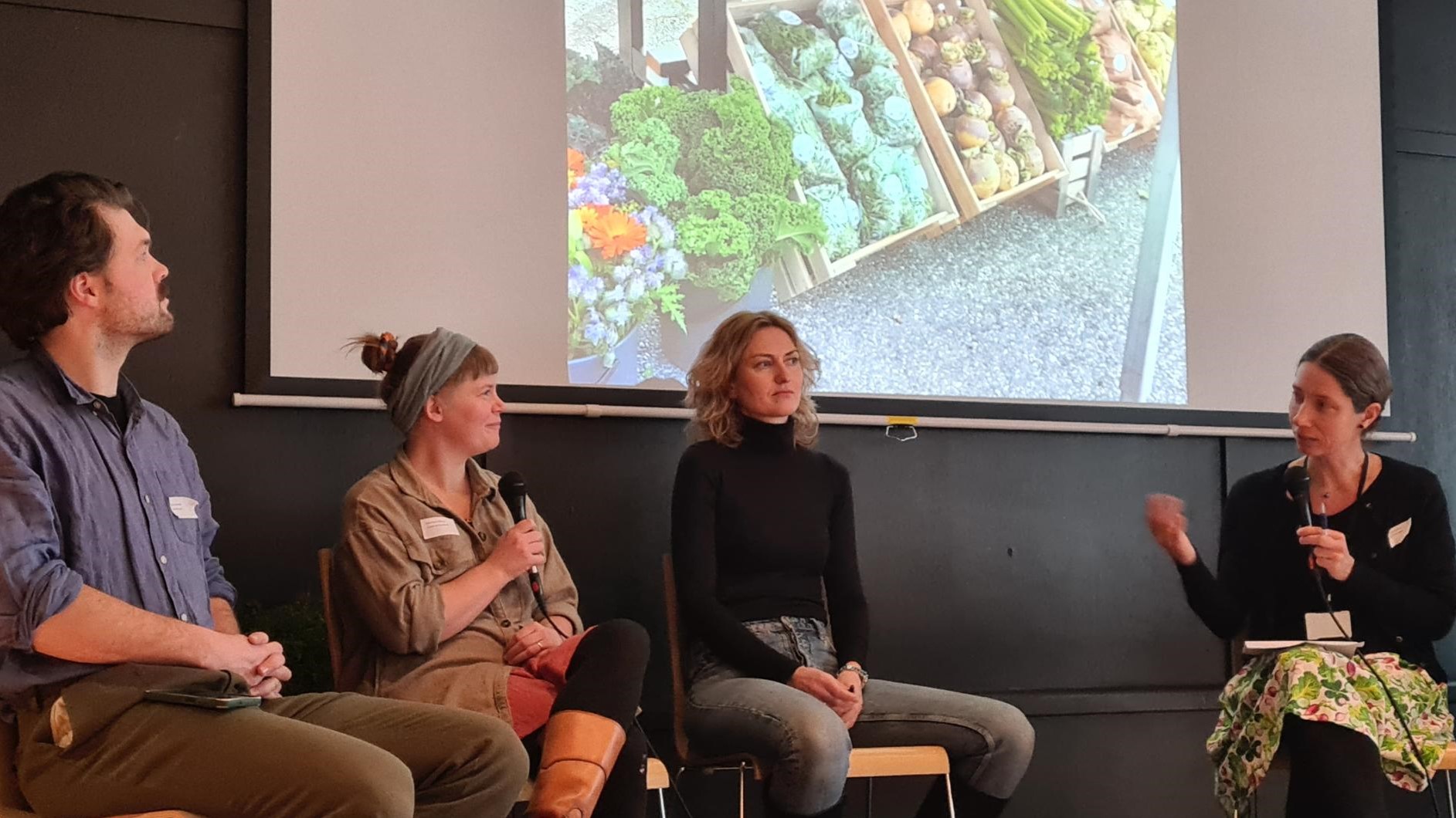 Småskala grøntprodusenter fra hele landet satt i panelsamtalen som ble ledet av Randi L. Gjertsen fra Bondens marked Norge (t.h.). I produsentpanelet satt Ida Kleppe fra Lundemannsverk på Stord, Sofia Maria Bang Elm fra Lesja og Sigurd Vassenden fra Grønt frå Grindal i Trøndelag (t.v) . Alle med minst 2-5 års salgsproduksjon fra markedshagedrift. Foto: Frøydis Lindén / SFVL. Fire mennesker som sitter på stoler foran en skjerm med et bilde av grønnsaker i kasser